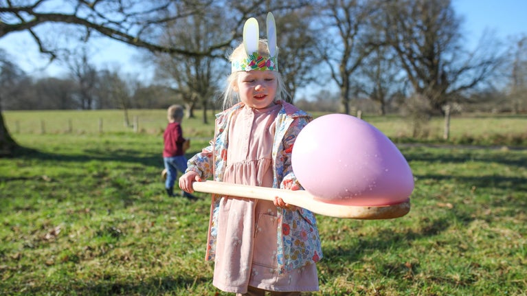 A little girl wearing bunny ear holding a giant egg and spoon